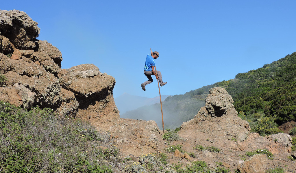 Persona usando un garrote para saltar entre rocas en un paisaje de Tenerife.