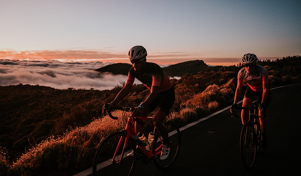 Ciclistas en carretera con paisaje montañoso al atardecer en Tenerife.