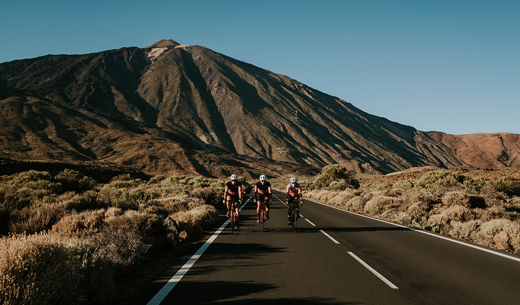 Ciclistas en carretera hacia el Teide, Tenerife, con la montaña al fondo.