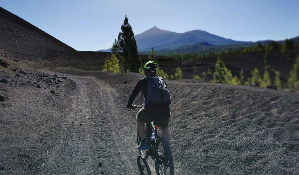 Ciclista en sendero volcánico con el Teide al fondo en Tenerife.