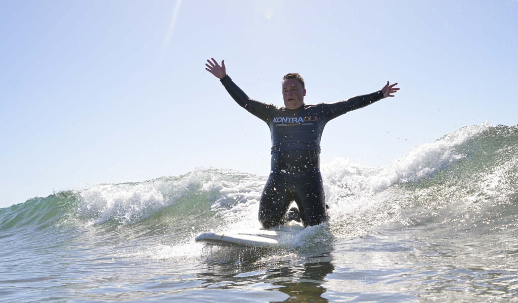 Surfero sobre ola con brazos extendidos, camiseta de Kontraola. Surf en Tenerife.