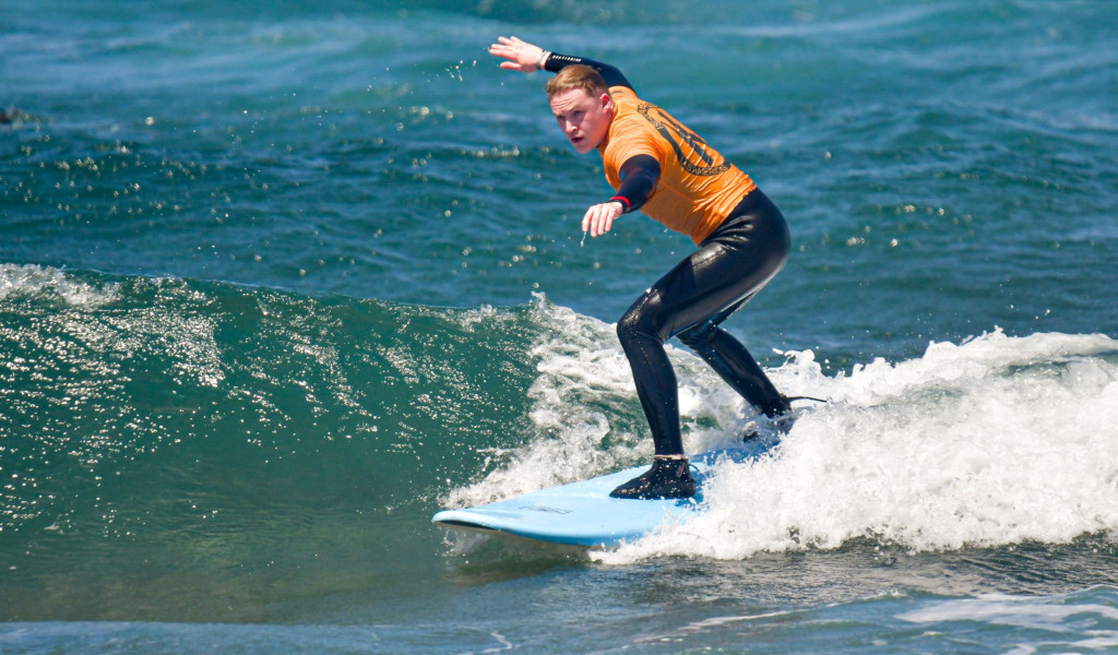 Persona surfeando una ola en Tenerife, vistiendo traje de neopreno naranja.