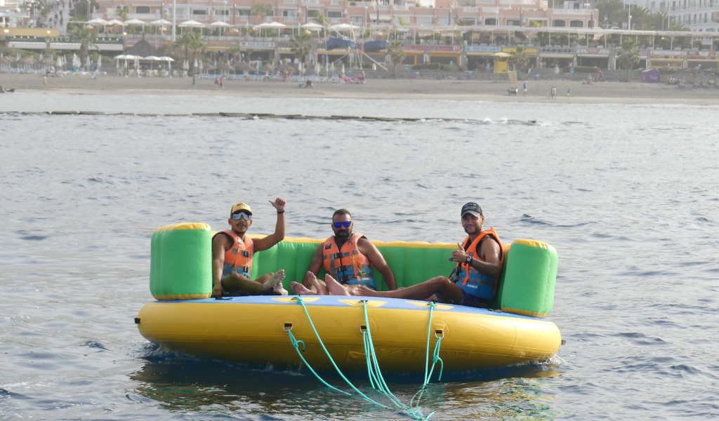 Tres personas en una plataforma inflable en el mar, Playa de las Américas al fondo, Tenerife.
