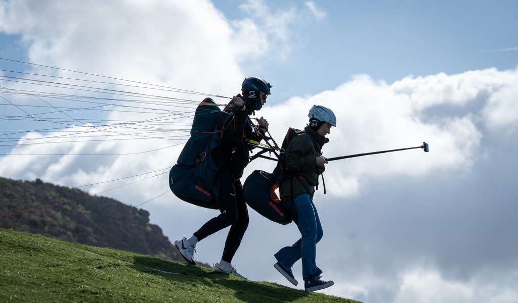 Dos personas despegando en parapente en Tenerife bajo un cielo nublado.