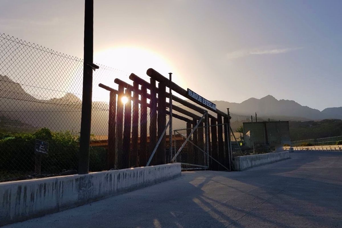Entrada cercada al Parque Estelar de Tenerife con montañas al fondo y el sol brillando.