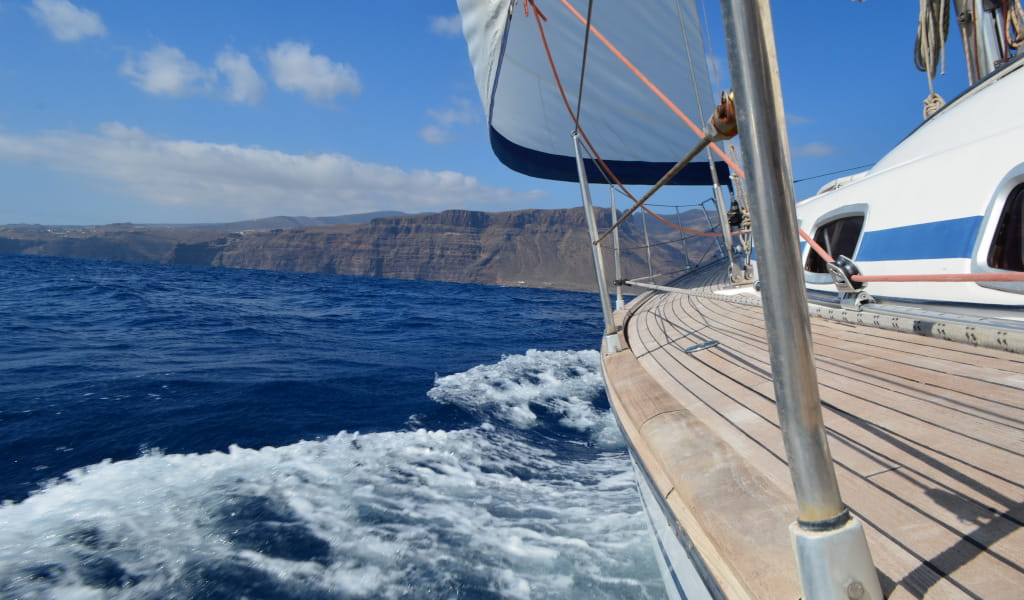 Velero navegando cerca de la costa de Tenerife con montañas al fondo.