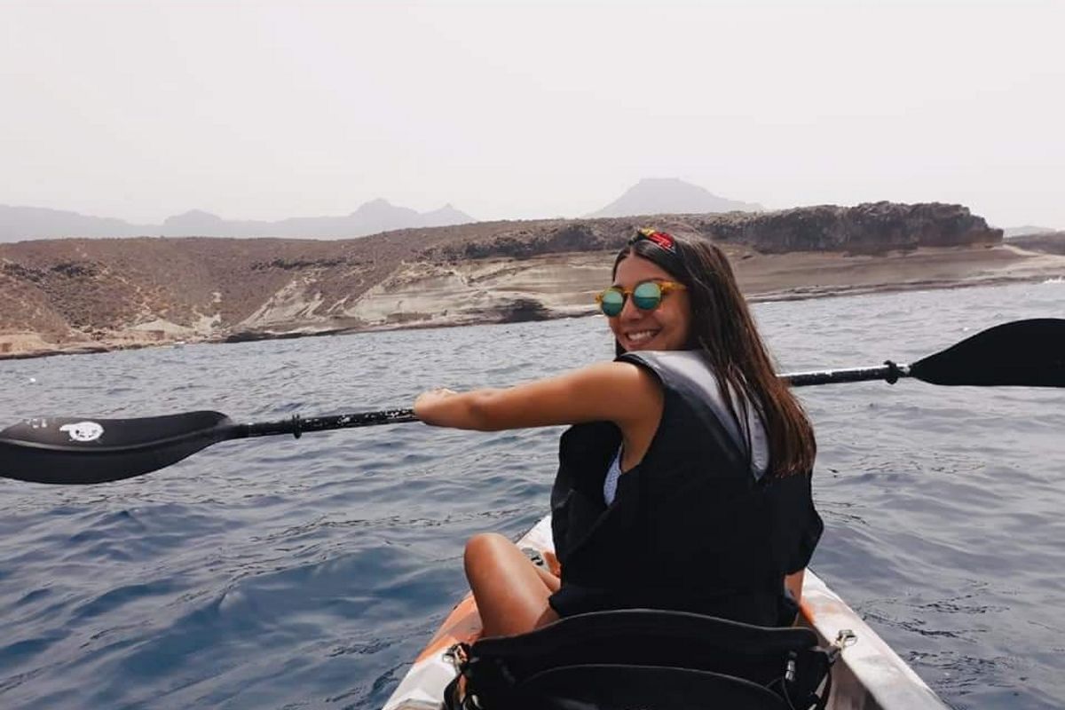 Persona remando en kayak en aguas de Tenerife, con paisaje montañoso al fondo.
