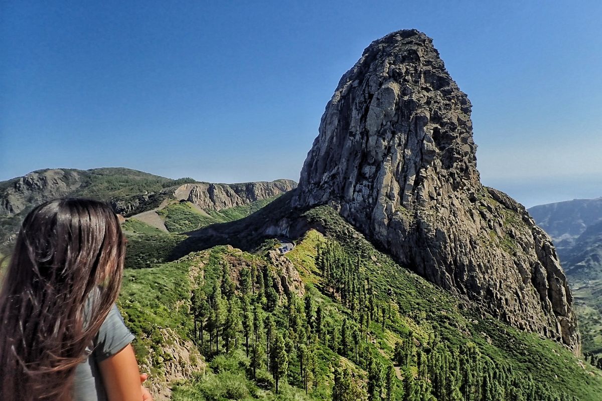 Mujer observando el Roque de Agando en Tenerife, rodeado de vegetación.