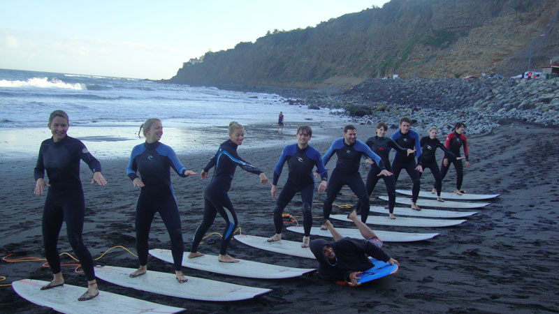 Grupo de personas aprende a surfear en la playa de Tenerife, alineados sobre tablas.