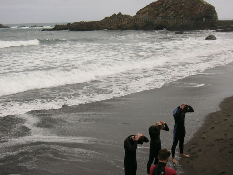 Personas en trajes de neopreno en la playa El Roque de las Bodegas, Tenerife.