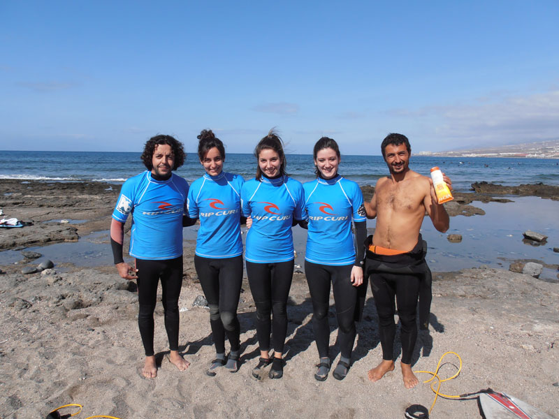 Grupo de surfistas en la playa de Tenerife con trajes de neopreno azules.