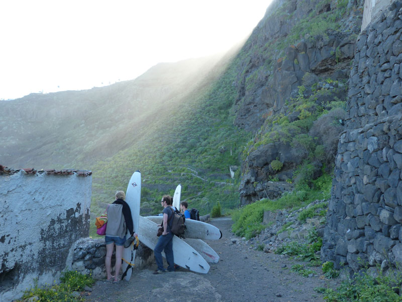 Personas con tablas de surf caminando por un sendero en Tenerife, rodeado de montañas.