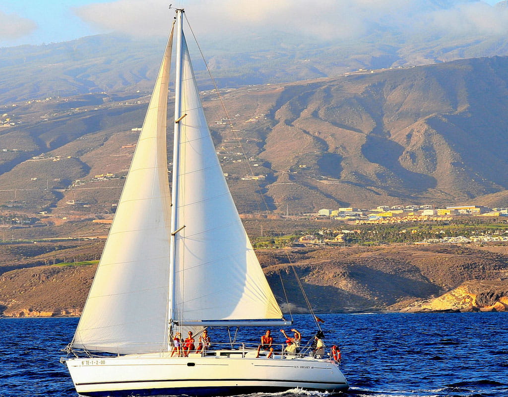 Velero navegando cerca de la costa de Tenerife con montañas al fondo.