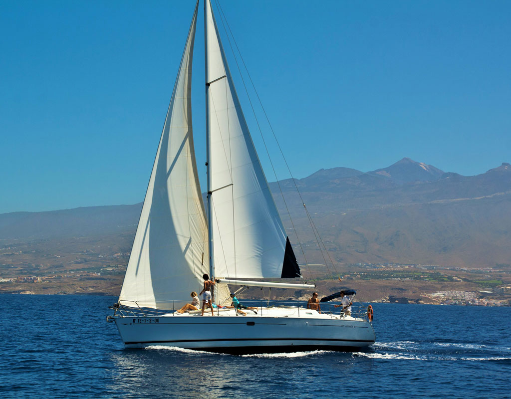 Velero navegando frente a la costa de Tenerife con montañas al fondo.