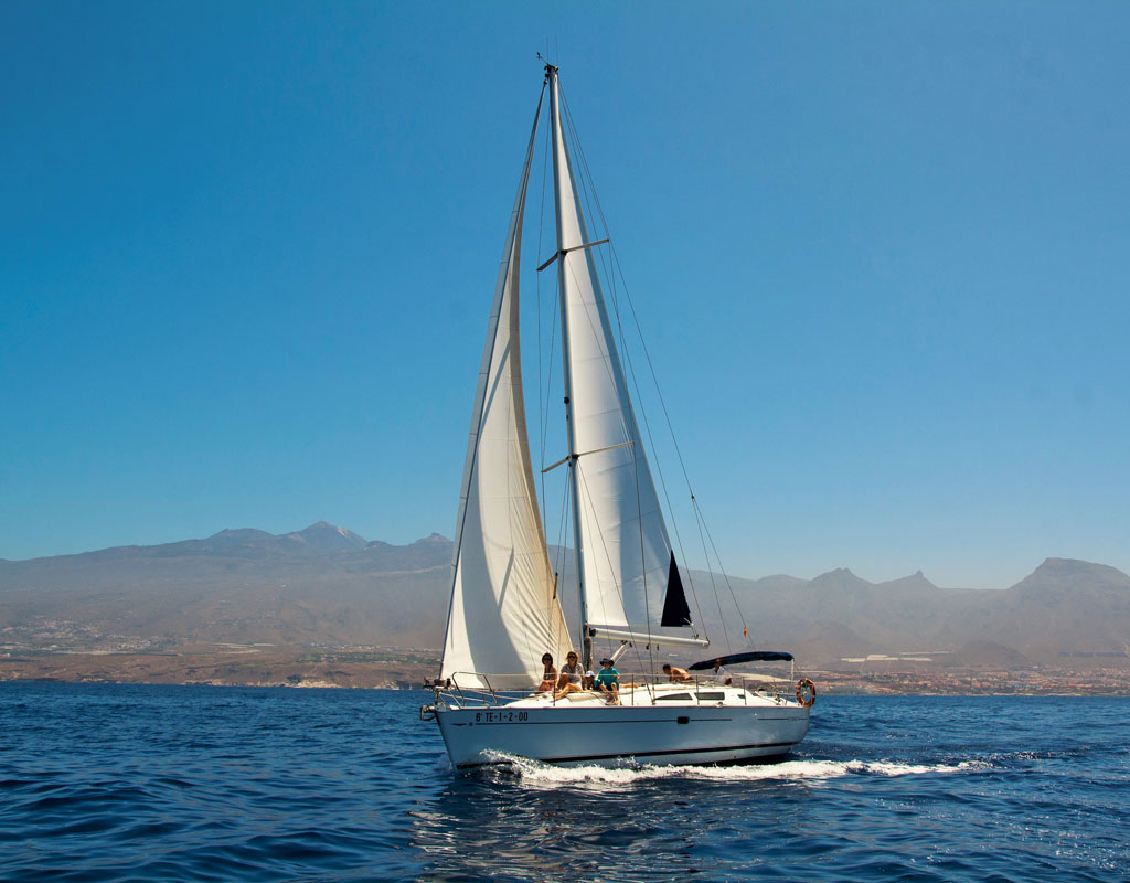 Velero navegando frente a la costa de Tenerife con montañas al fondo.