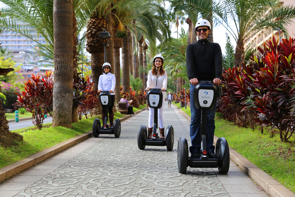 Tres personas en segways pasean por una avenida bordeada de palmeras en Tenerife.