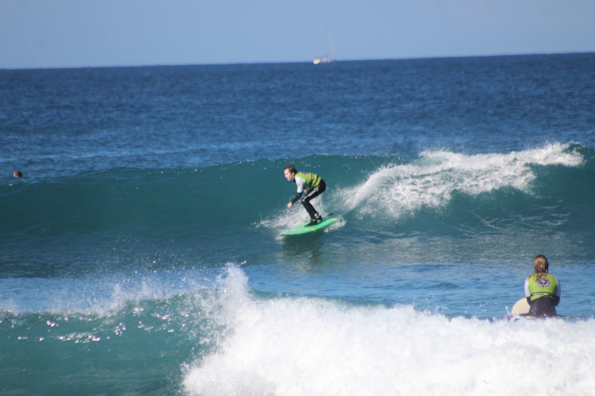 Surfista montando una ola en Tenerife, con otra persona observando desde el agua.