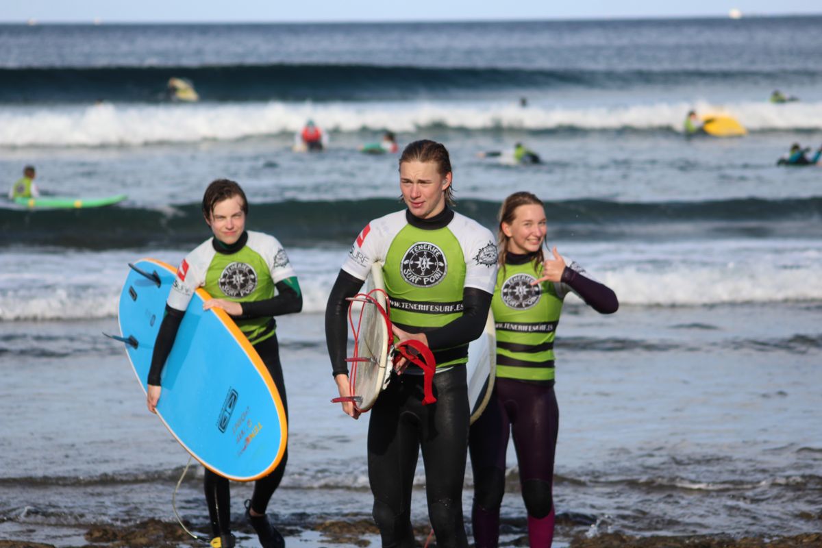 Surfistas en la playa de Tenerife, con tablas y trajes de neopreno, cerca del mar.
