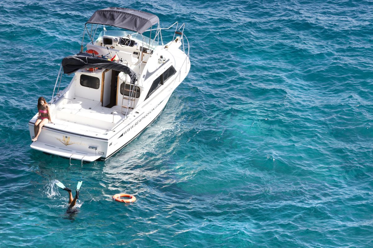 Barco con joven a bordo y persona buceando en el mar de Tenerife.