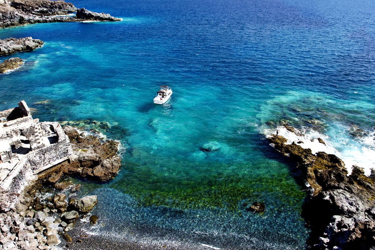 Barco navegando en aguas cristalinas cerca de la costa rocosa de Tenerife.