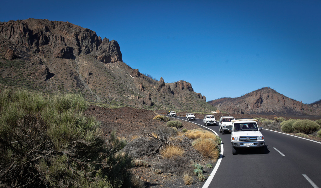 Caravana de coches en carretera hacia el Teide, Tenerife, rodeada de montañas.