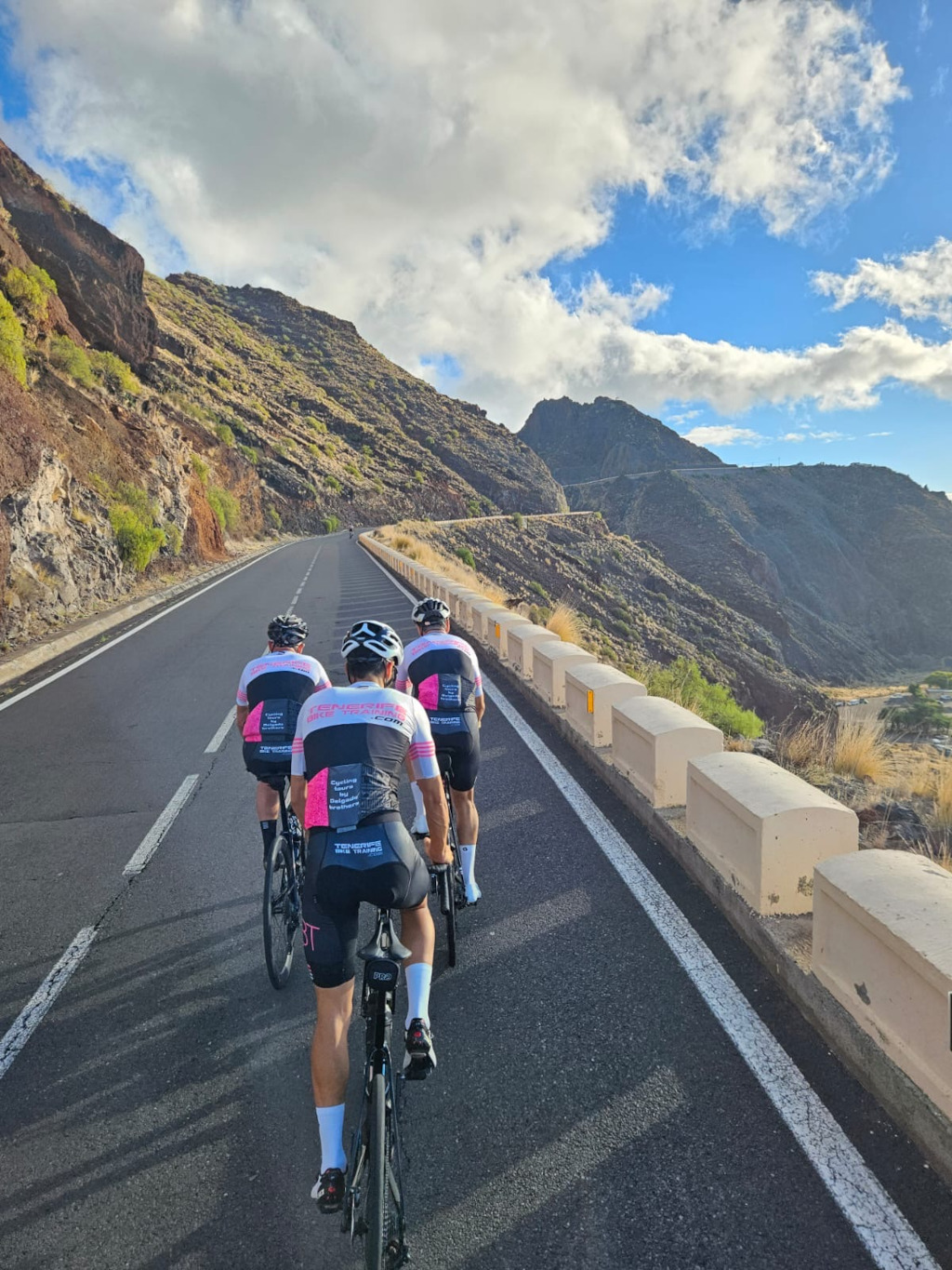 Ciclistas subiendo una carretera montañosa en Tenerife bajo cielo parcialmente nublado.