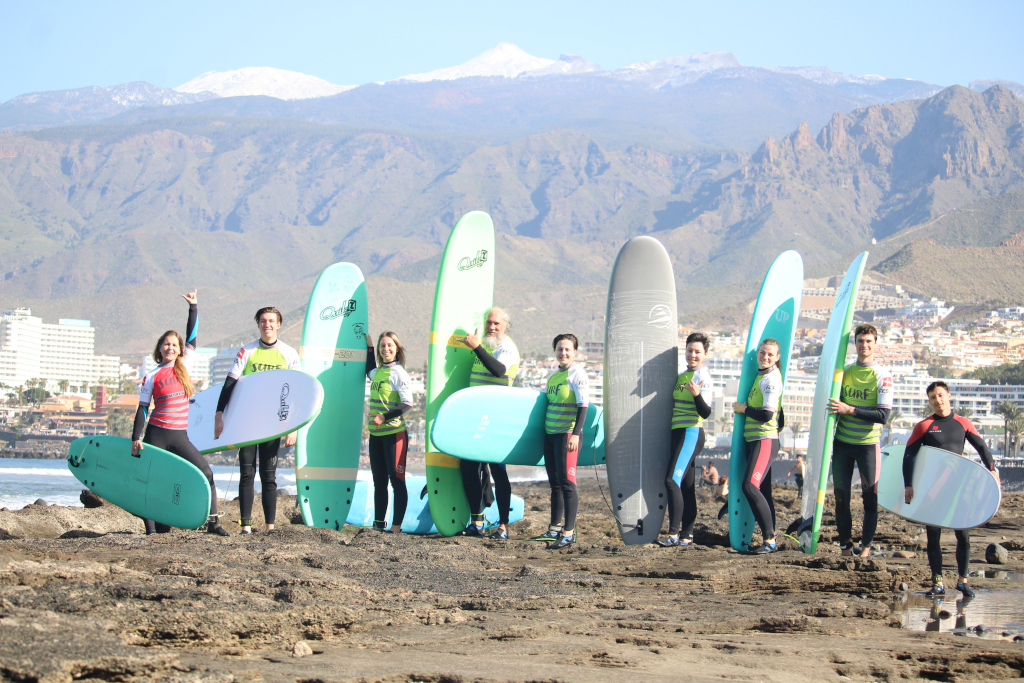 Grupo de surfistas con tablas en la playa de Tenerife, montañas al fondo.