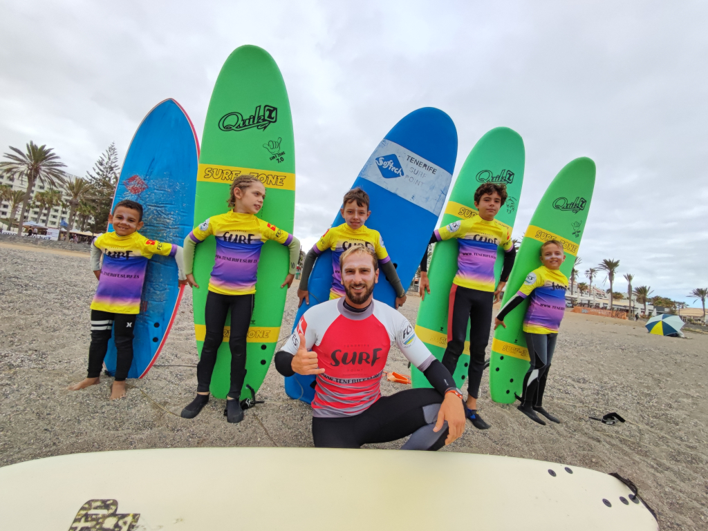 Instructor de surf con niños sosteniendo tablas en playa de Tenerife.