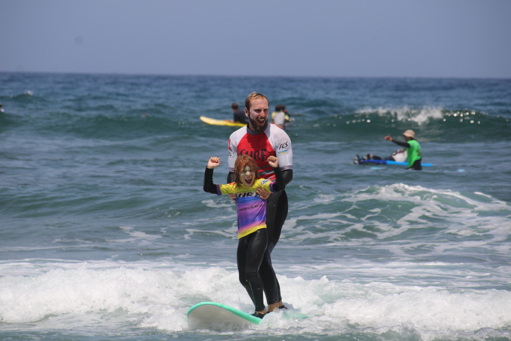 Surfista adulto y niño en clase de surf en una playa de Tenerife.
