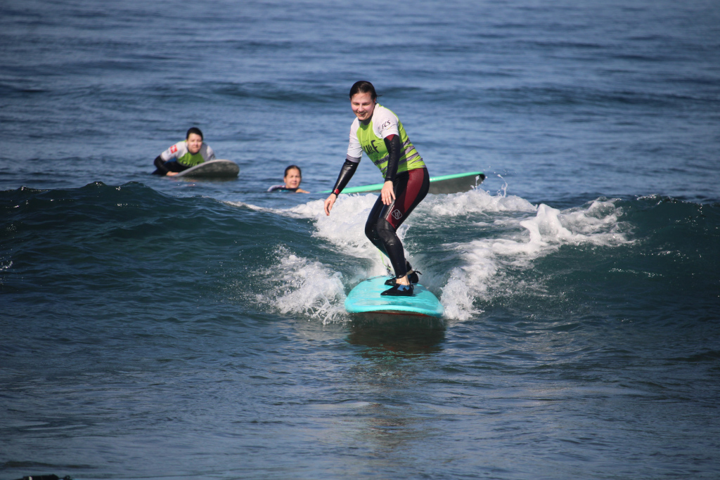 Surfista montando una ola en Punta del Hidalgo, Tenerife, con dos personas al fondo.