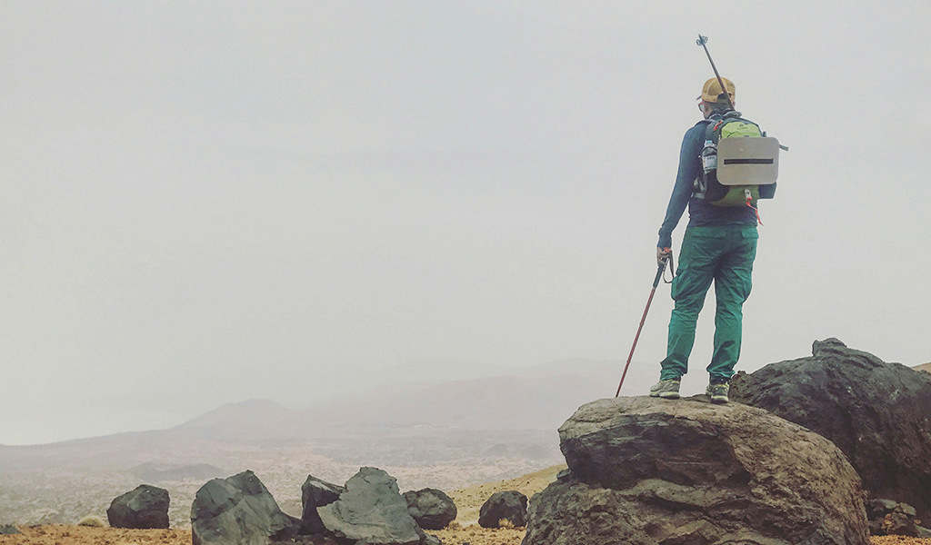 Persona de pie sobre roca con equipo de senderismo en paisaje árido de Tenerife.
