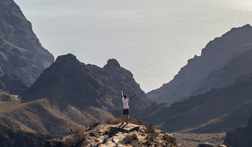 Persona con los brazos levantados en un mirador en un paisaje montañoso de Tenerife.
