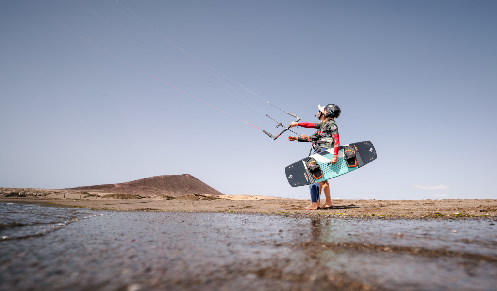 Persona practicando kitesurf en Playa El Médano, Tenerife, con cerro al fondo.