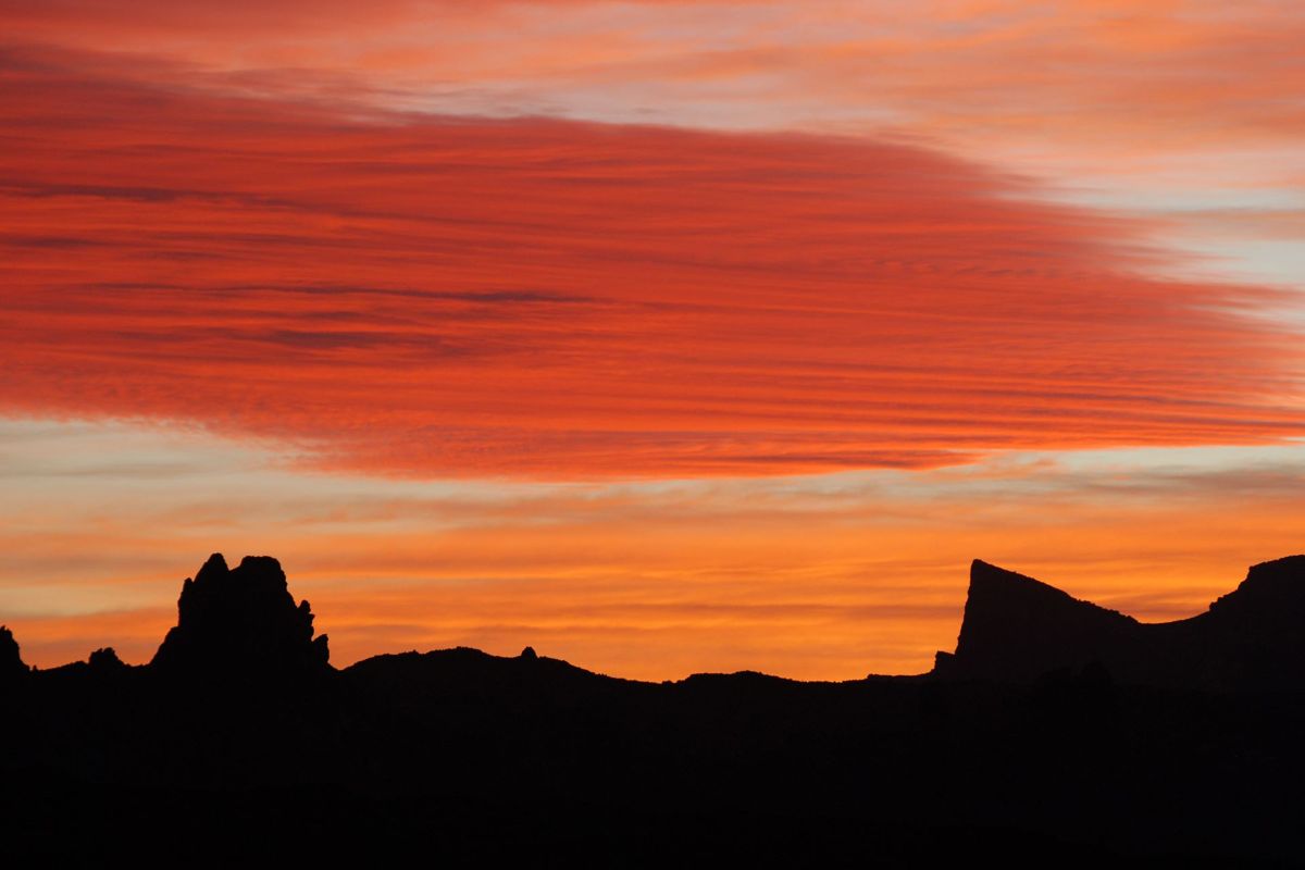 Atardecer sobre montañas en Tenerife con nubes rojas y cielo anaranjado.