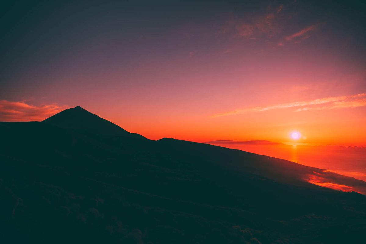Amanecer sobre el Teide en Tenerife con cielo rojo y sol en el horizonte.