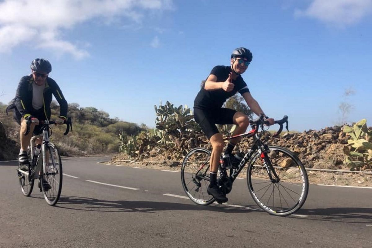 Ciclistas en carretera cerca de cactus en Tenerife bajo cielo despejado.