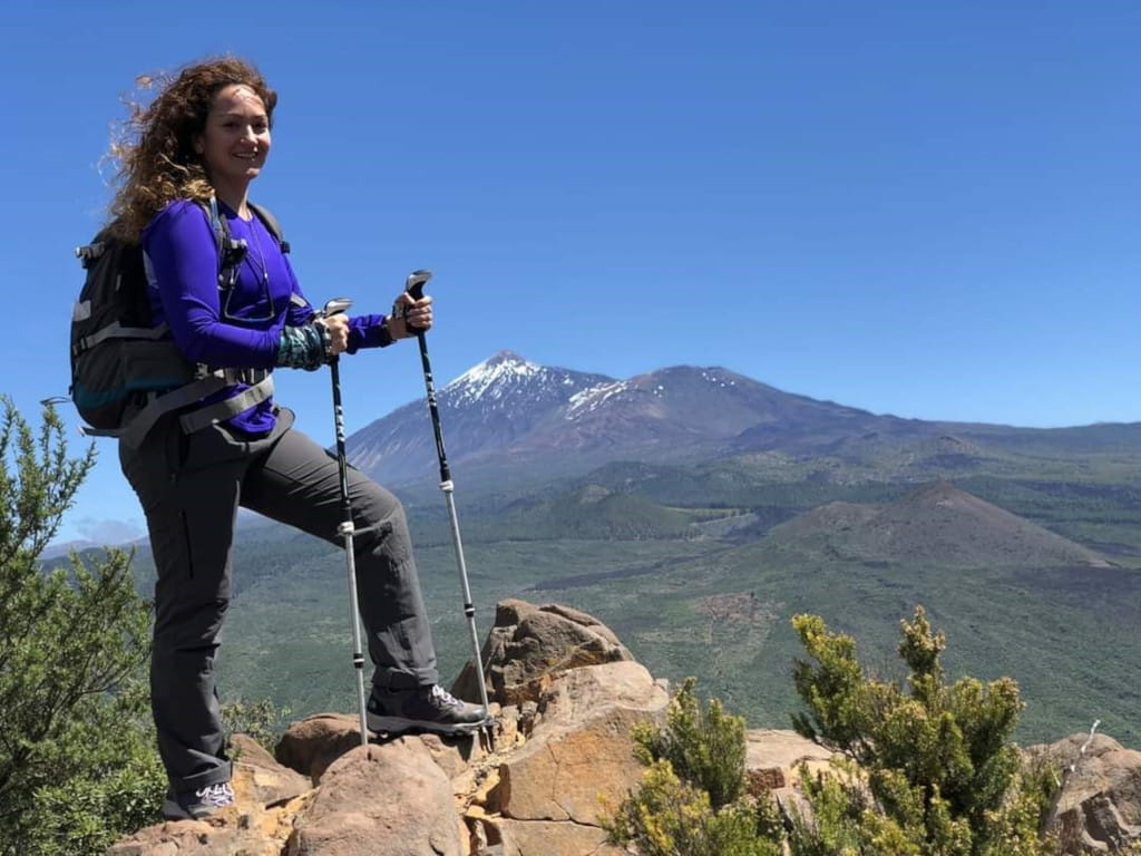 Excursionista con bastones en camino rocoso con el Teide al fondo, Tenerife.
