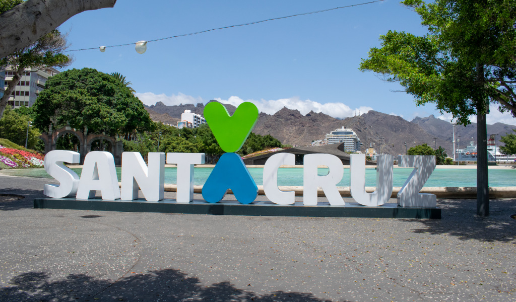 Letrero Santa Cruz en plaza con árboles y montañas al fondo.