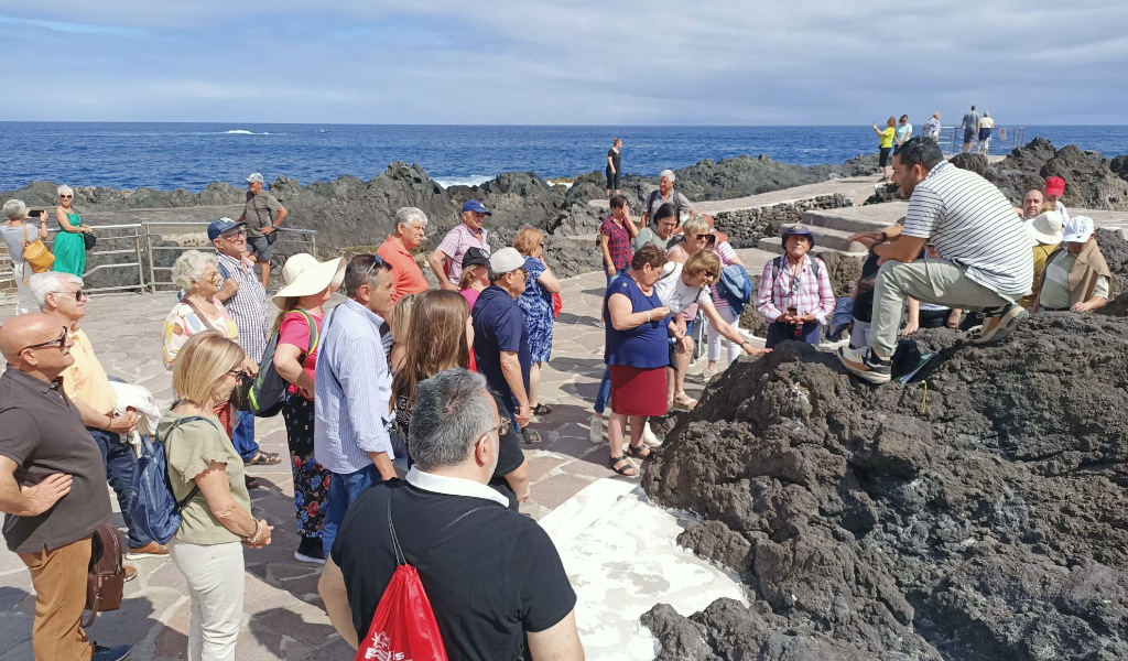 Grupo de personas escucha a un guía sobre rocas volcánicas en el Puerto de la Cruz, Tenerife.