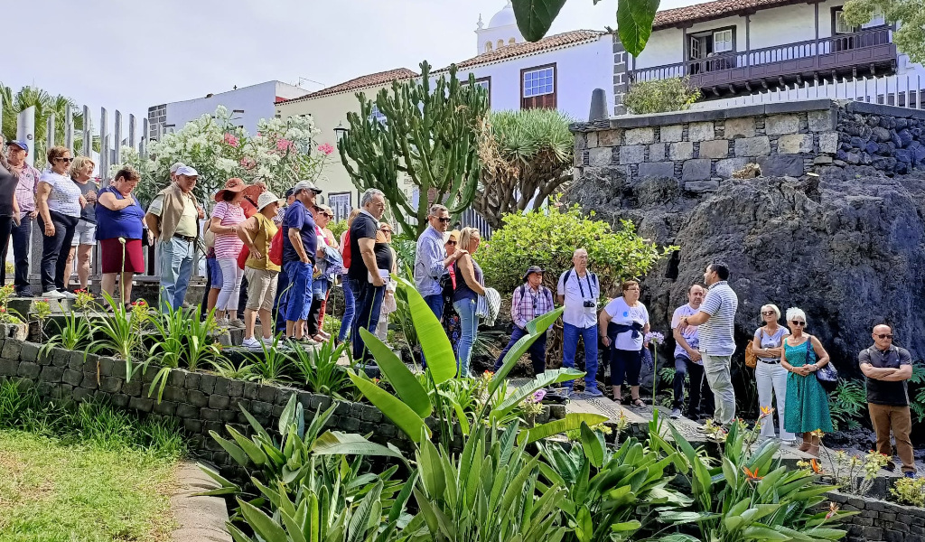Grupo de personas recorriendo un jardín en un lugar de Tenerife, rodeados de plantas y arquitectura local.
