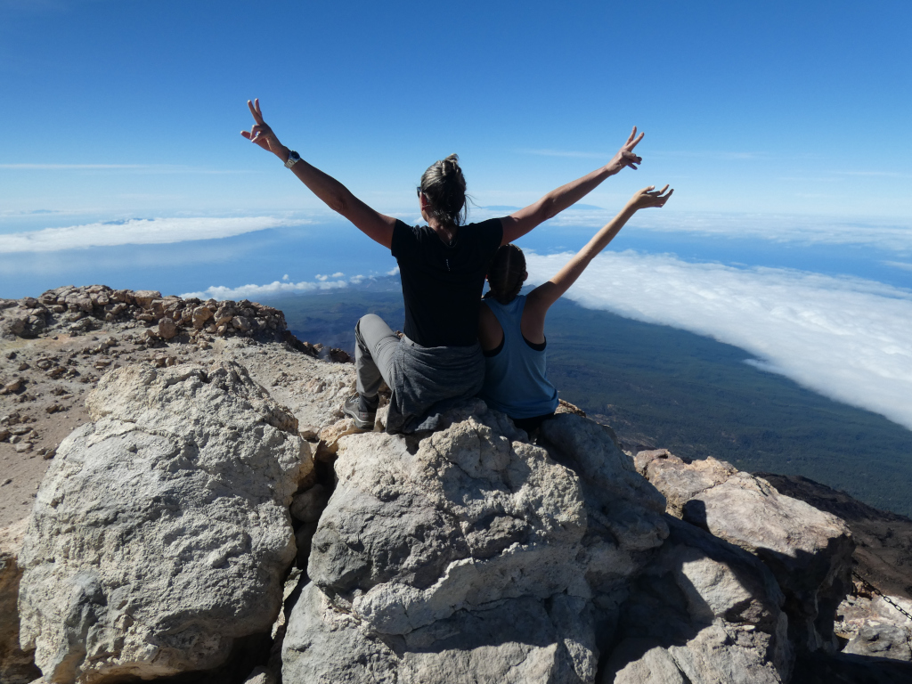 Personas levantando los brazos en la cima del Teide en Tenerife, con vistas al paisaje nuboso.