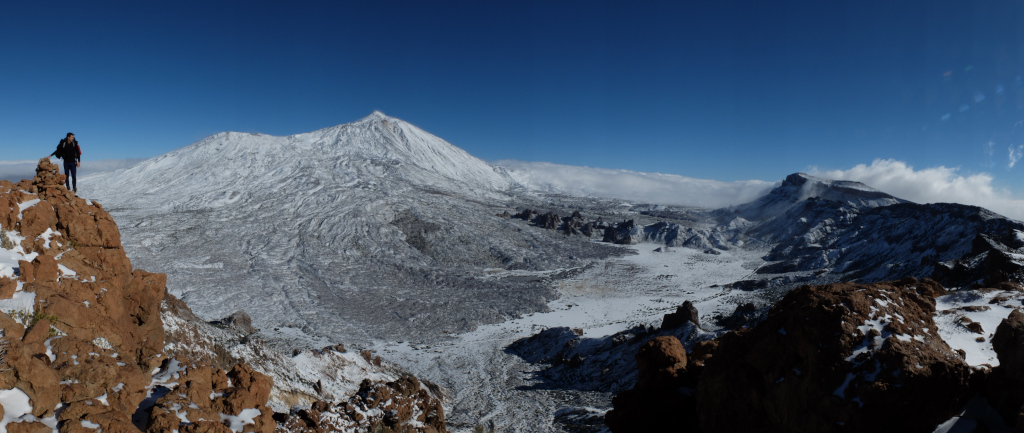 Paisaje nevado del Teide en Tenerife con un excursionista en la cima de una roca.