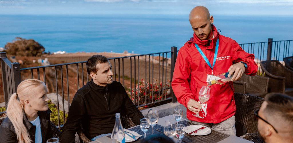 Mesero sirviendo vino a turistas en terraza con vista al mar en Tenerife.