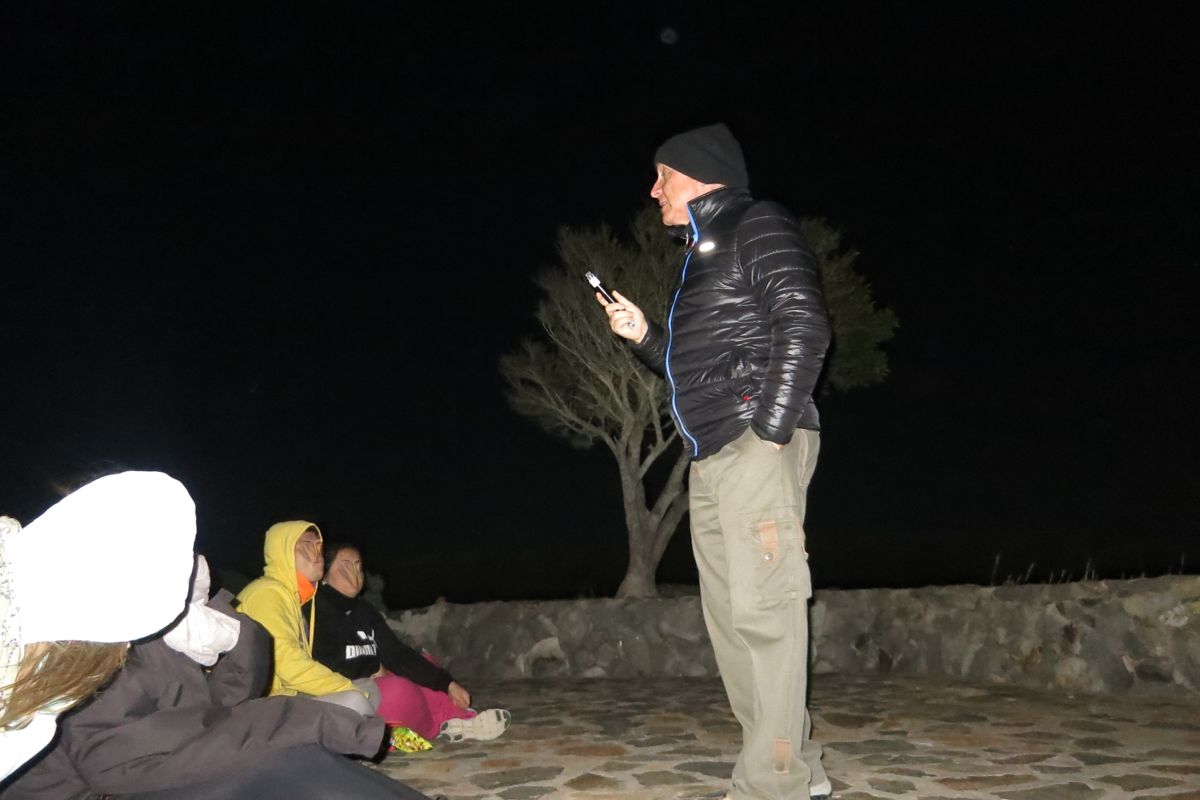 Persona hablando al aire libre en la noche en Tenerife, con grupo sentado cerca.