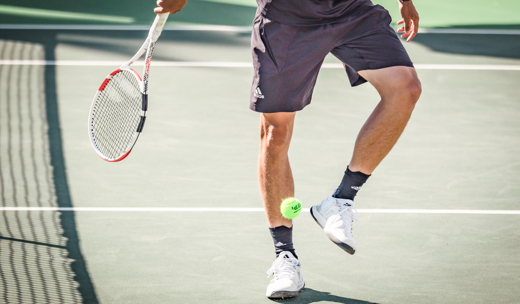 Jugador de tenis en una cancha en Tenerife, golpeando una pelota con su raqueta.