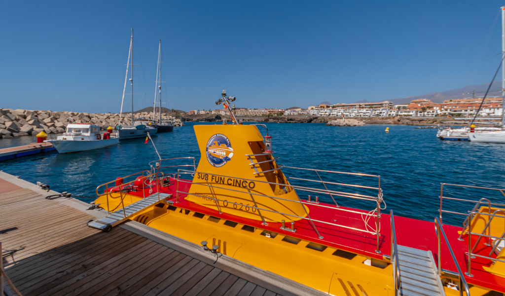 Submarino amarillo atracado en el puerto de Puerto de la Cruz, Tenerife, con barcos al fondo.