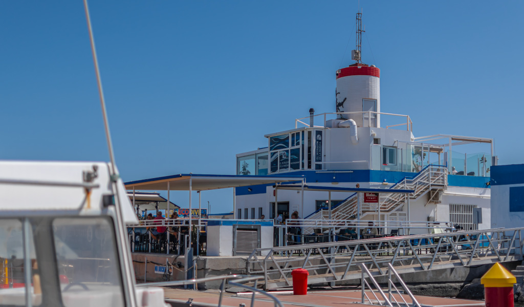 Edificio blanco y azul con faro rojo en Santa Cruz de Tenerife, visto desde un muelle.