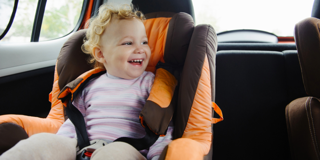 Niño sonriendo en una silla de auto dentro de un coche.