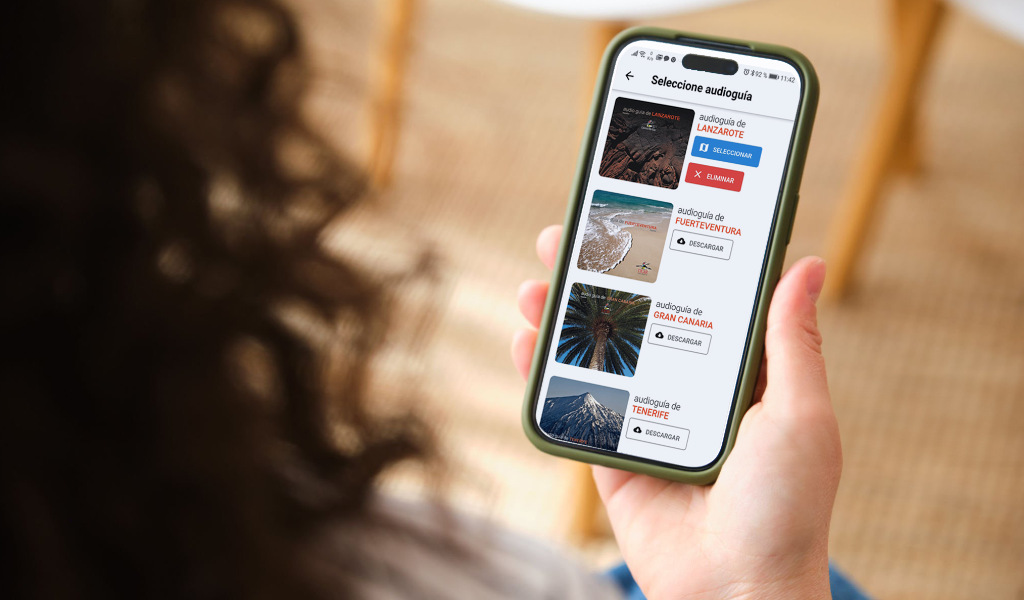 Persona sosteniendo un móvil con audio guías de Lanzarote, Fuerteventura, Gran Canaria y Tenerife.