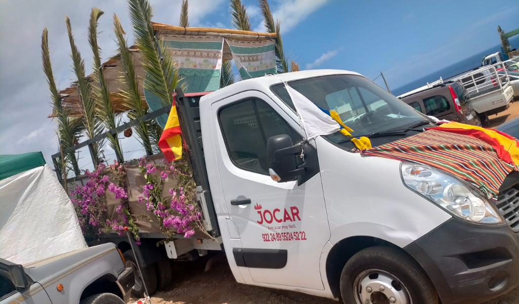 Camión decorado con flores y banderas en Tenerife, con vista parcial al mar.